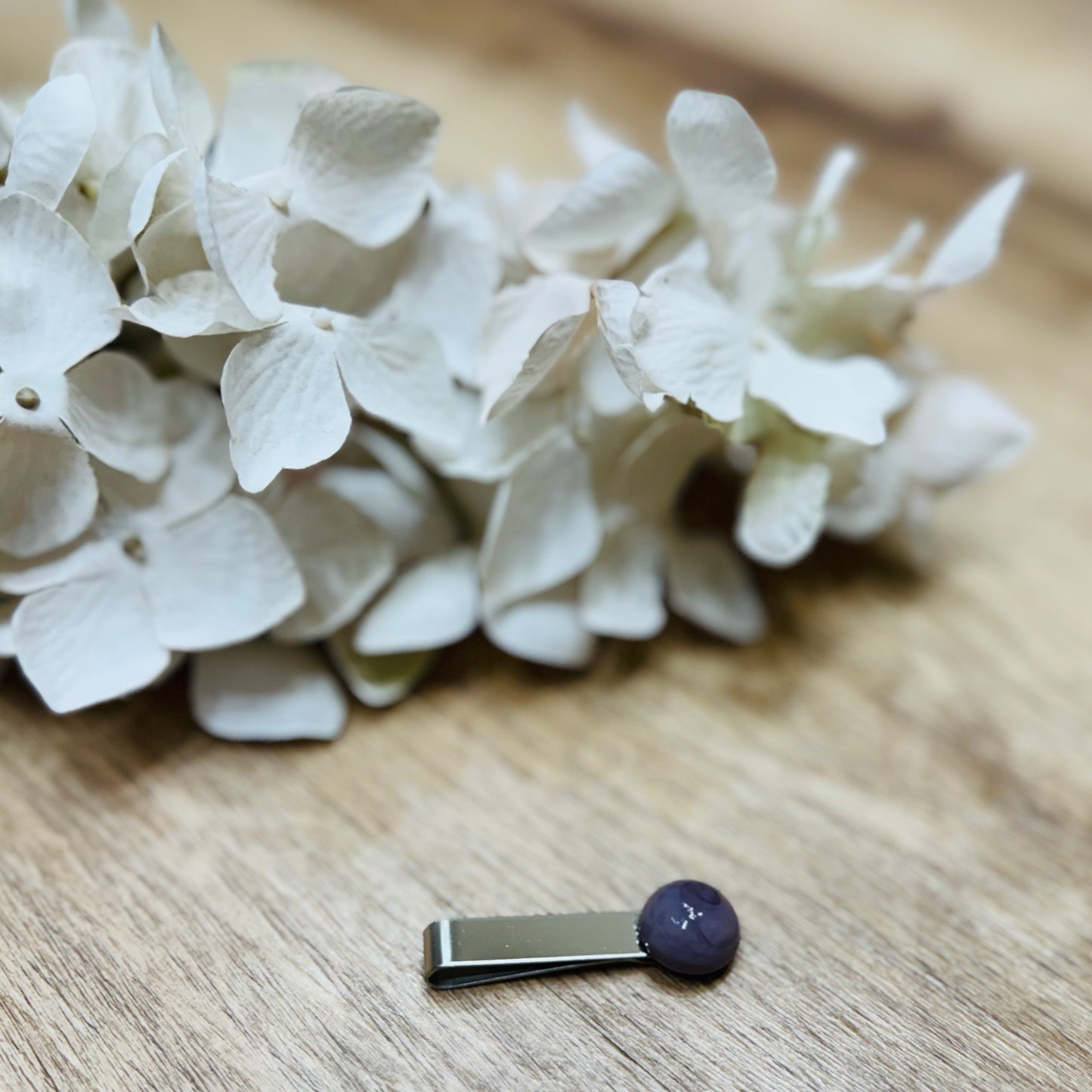 Un fermacravatta colorato vicino ad un fiore bianco su un tavolo di legno