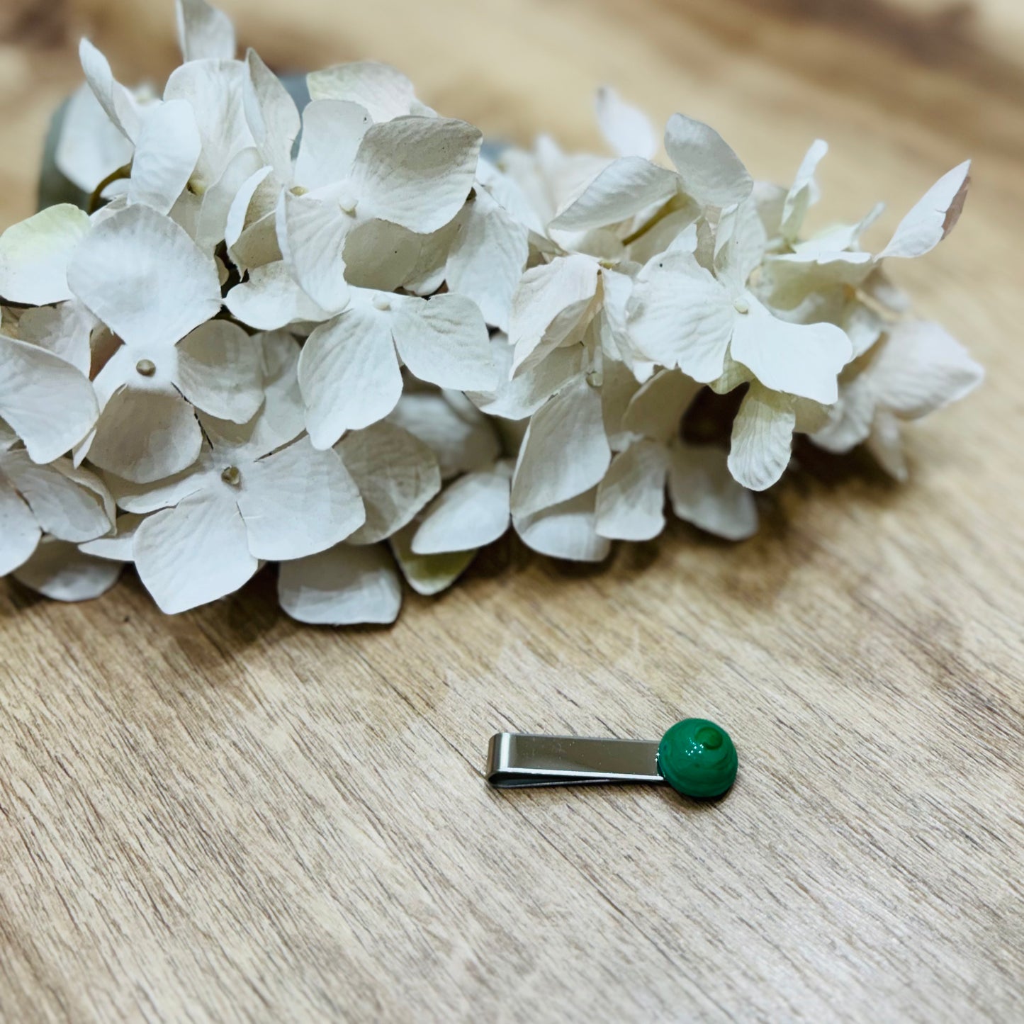 Un fermacravatta colorato vicino ad un fiore bianco su un tavolo di legno