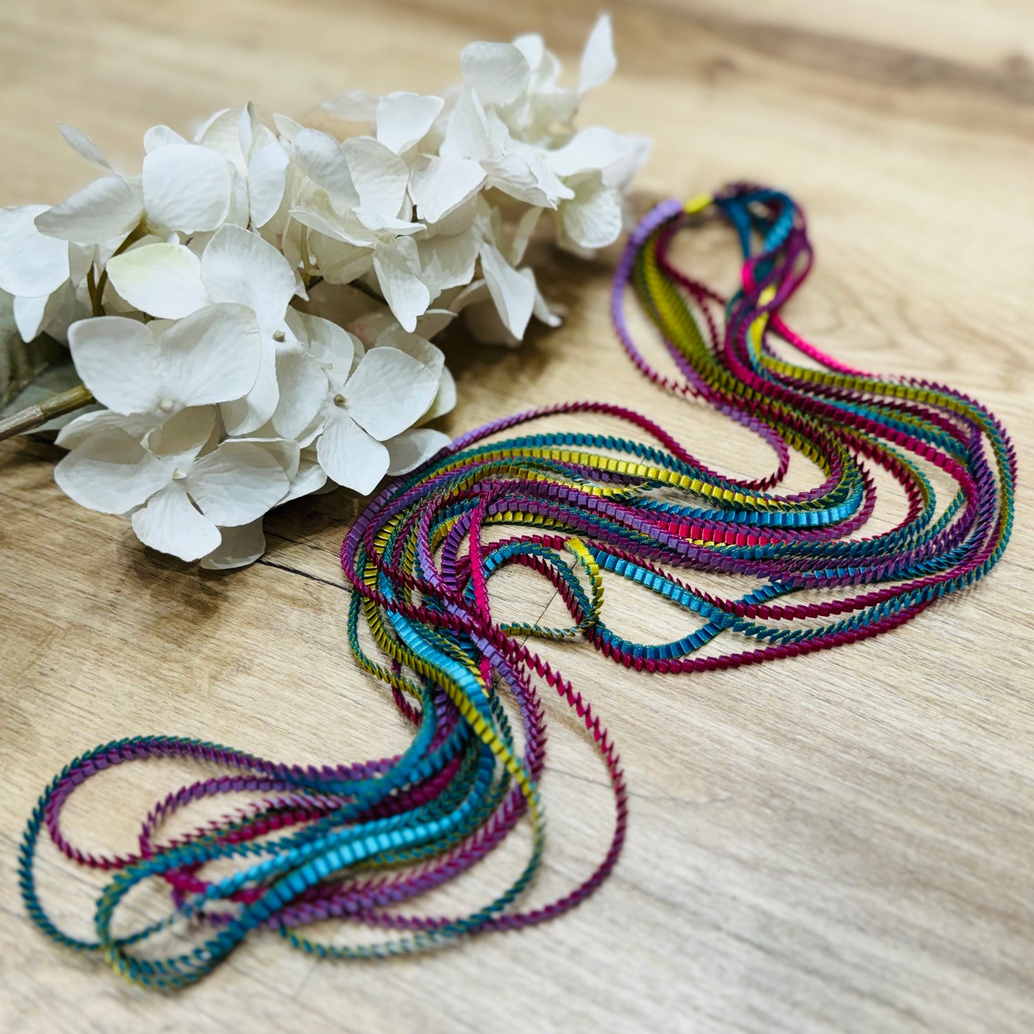 un mazzo di fiori posato su un tavolo di legno con vicino una collana multicolore