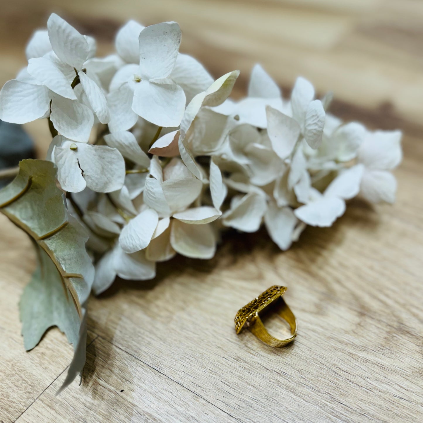 un mazzo di fiori bianchi posato su un tavolo di legno con vicino un anello