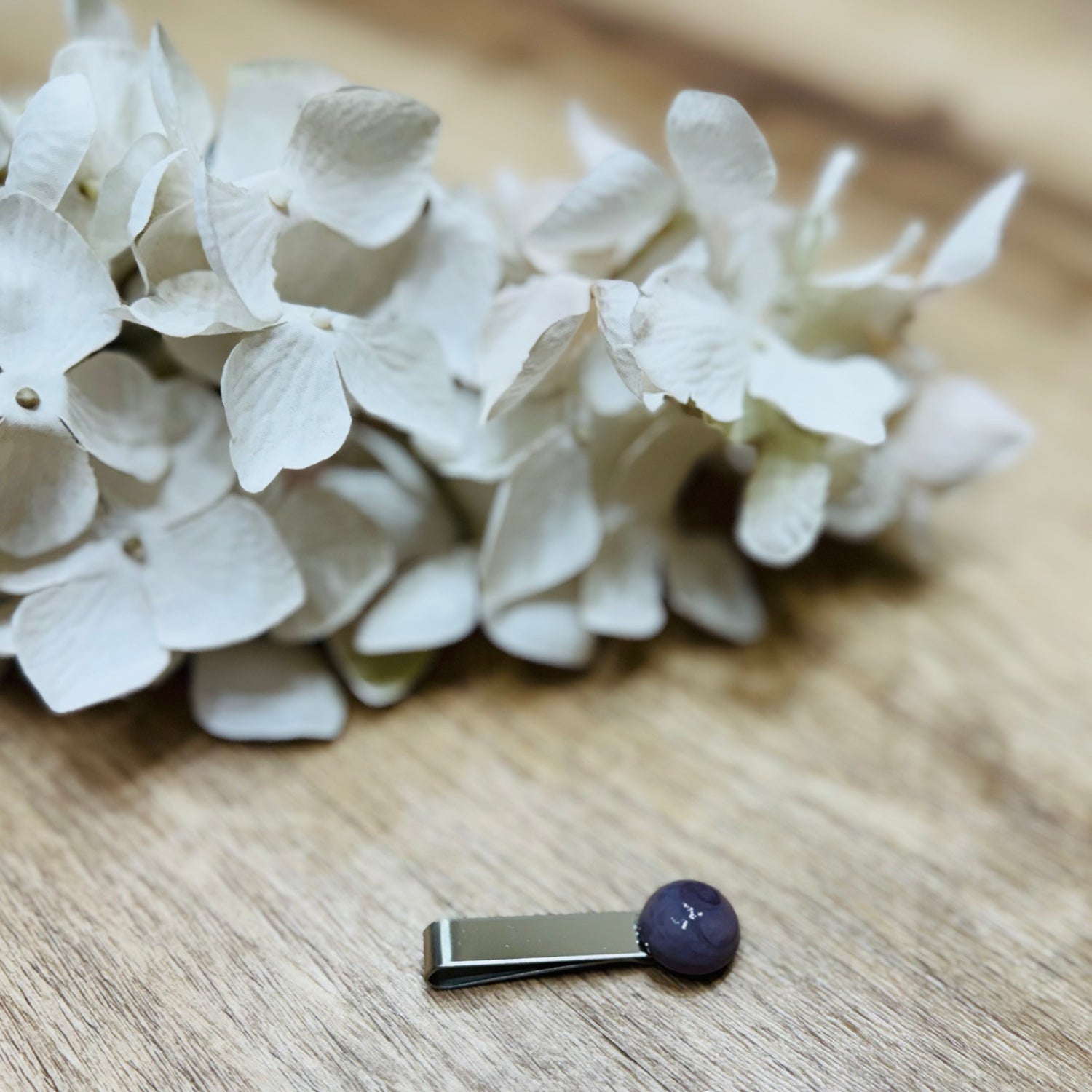 Un fermacravatta colorato vicino ad un fiore bianco su un tavolo di legno