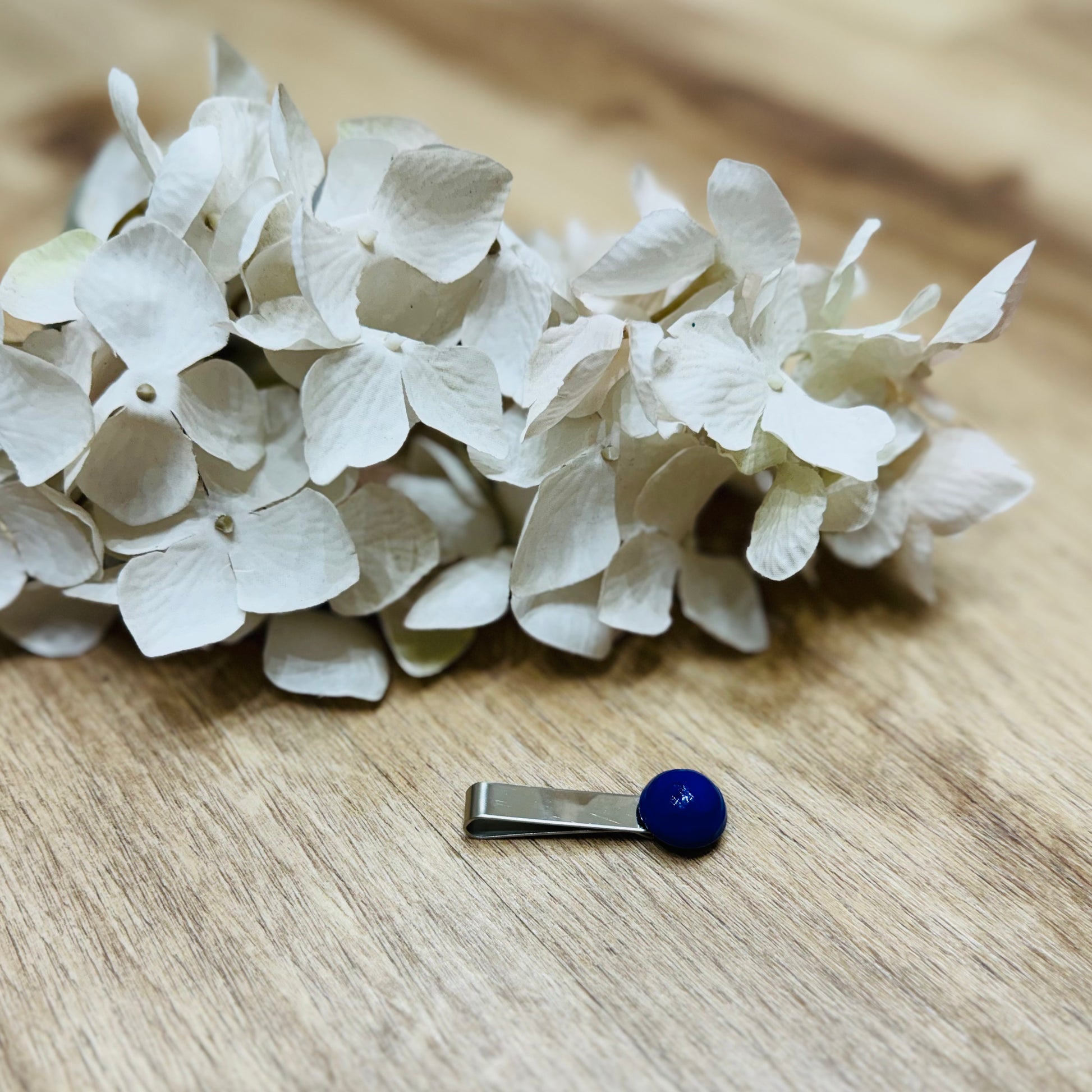 Un fermacravatta colorato vicino ad un fiore appoggiato su un tavolo di legno